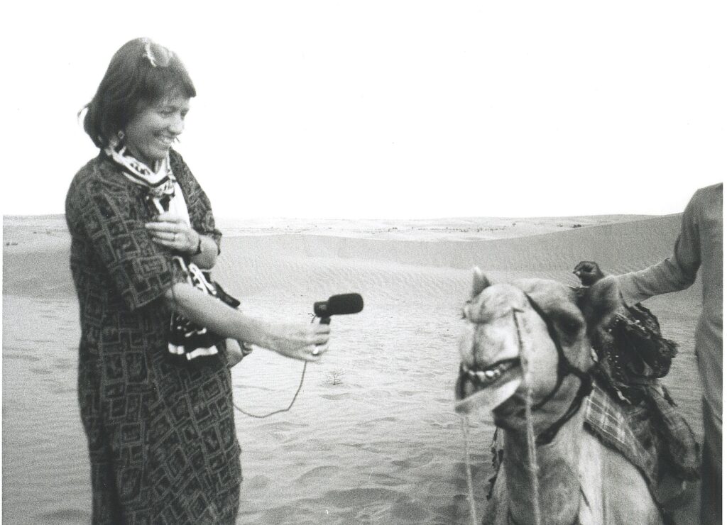 A photo of Hildegaard Westerkaamp smiling as she records a camel in the desert.