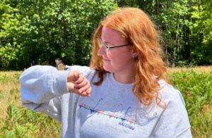A person wearing a sweatshirt is lifting their arm up to look at the monarch butterfly resting on their sleeve.